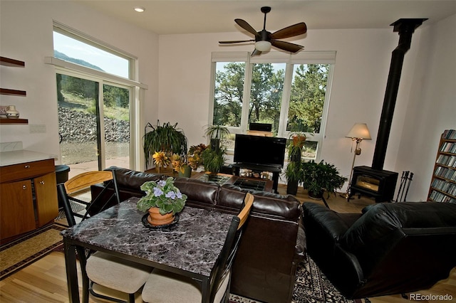 living room with light wood-type flooring, a wood stove, and ceiling fan