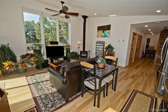 living room with ceiling fan, light wood-type flooring, a wood stove, and vaulted ceiling