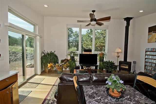 living room featuring a wood stove, a wealth of natural light, light hardwood / wood-style flooring, and ceiling fan