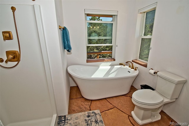 bathroom with a tub to relax in and toilet