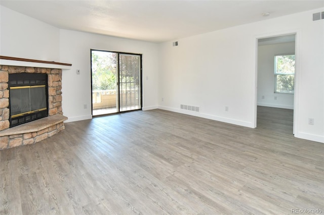 unfurnished living room featuring a healthy amount of sunlight, visible vents, a stone fireplace, and wood finished floors