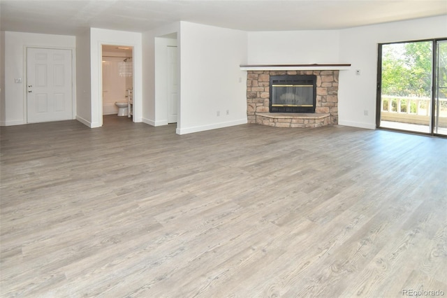 unfurnished living room with a stone fireplace, wood finished floors, and baseboards