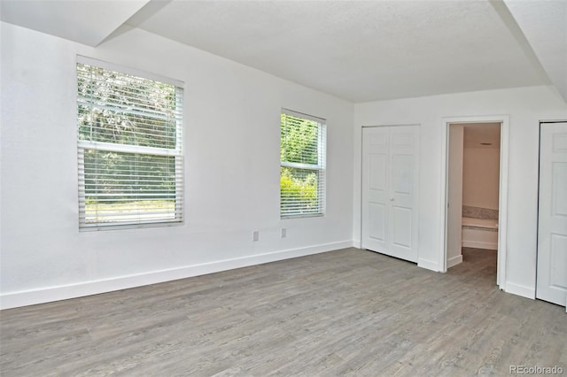 unfurnished bedroom with connected bathroom, baseboards, and wood finished floors