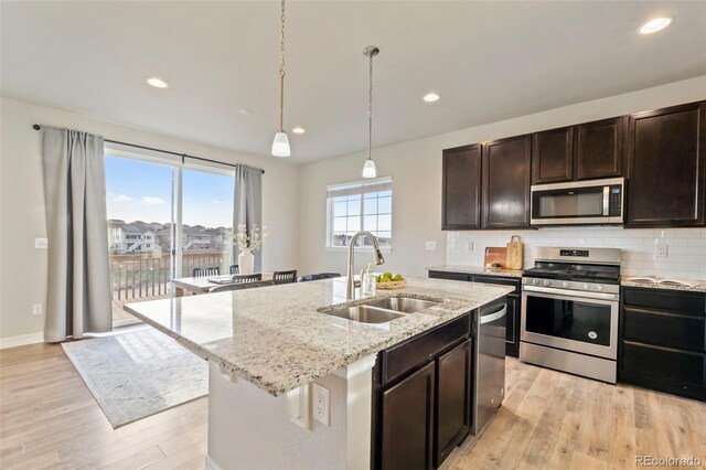 kitchen featuring light stone countertops, tasteful backsplash, a sink, light wood finished floors, and appliances with stainless steel finishes