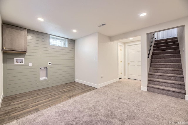 basement featuring light colored carpet and wooden walls