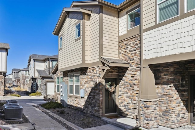 exterior space with a residential view, stone siding, an attached garage, and central AC unit