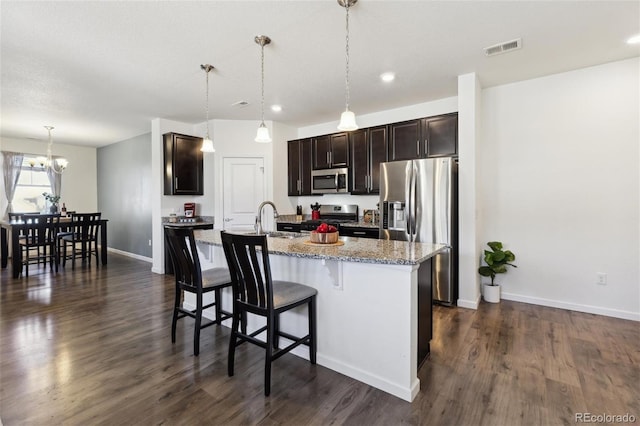 kitchen with a center island with sink, visible vents, appliances with stainless steel finishes, a kitchen breakfast bar, and dark wood-type flooring