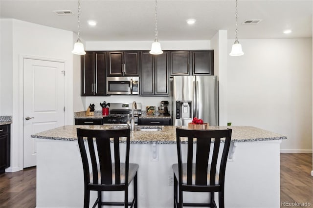 kitchen featuring visible vents, a center island with sink, appliances with stainless steel finishes, and a breakfast bar