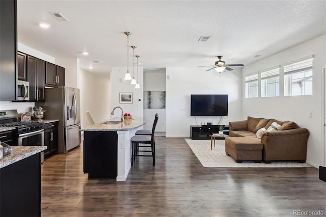 kitchen with visible vents, appliances with stainless steel finishes, a kitchen breakfast bar, light stone countertops, and a sink