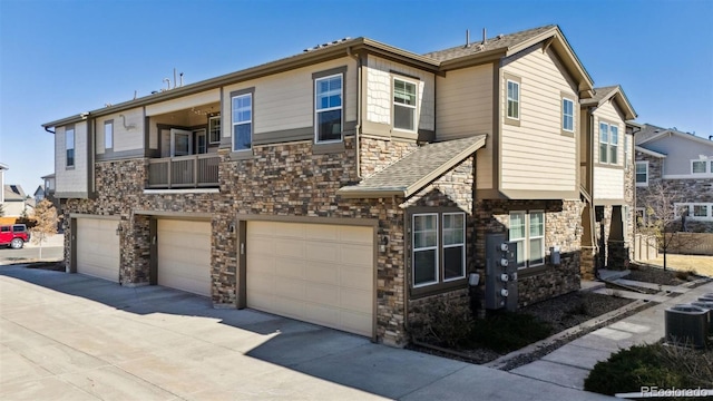 view of front of house with driveway, central AC unit, stone siding, roof with shingles, and an attached garage