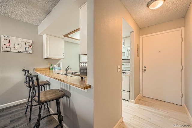 interior space featuring white cabinetry, sink, white appliances, wood counters, and a breakfast bar area