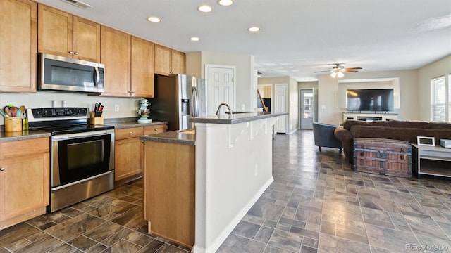 kitchen featuring a kitchen breakfast bar, dark tile patterned floors, a center island with sink, appliances with stainless steel finishes, and ceiling fan