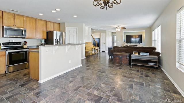 kitchen featuring ceiling fan, a kitchen bar, stainless steel appliances, and dark tile patterned floors