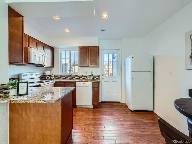 kitchen with white appliances, dark wood-type flooring, light stone counters, and a healthy amount of sunlight