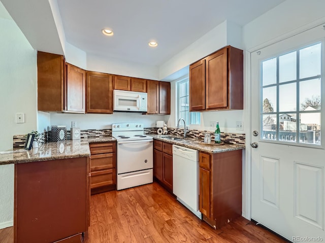 kitchen with white appliances, sink, light stone countertops, light wood-type flooring, and kitchen peninsula