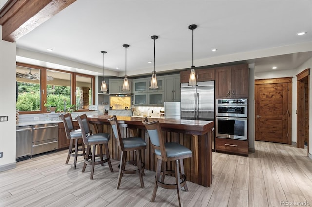 kitchen featuring a center island, hanging light fixtures, light hardwood / wood-style floors, decorative backsplash, and appliances with stainless steel finishes