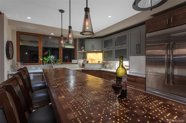 kitchen featuring backsplash, stainless steel built in fridge, hanging light fixtures, and black electric stovetop