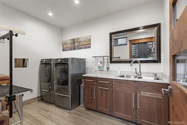 clothes washing area featuring cabinets, washer and clothes dryer, light hardwood / wood-style floors, and sink