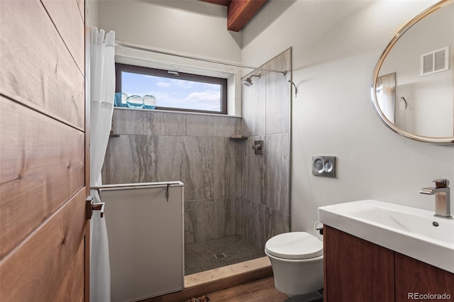 bathroom featuring beamed ceiling, a tile shower, vanity, and toilet