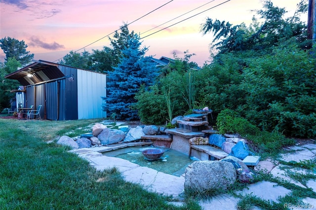 yard at dusk with a fire pit and a storage unit