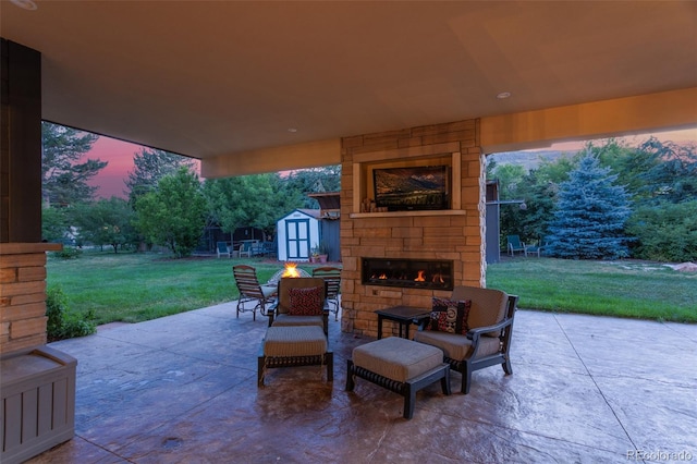 patio terrace at dusk with an outdoor stone fireplace, a yard, and a storage shed