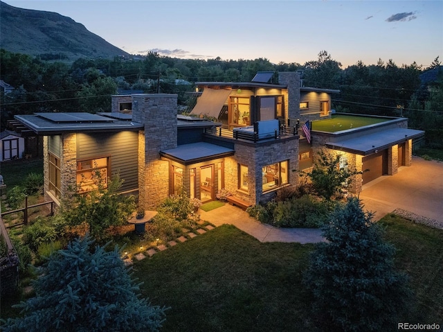 view of front of home with solar panels, a mountain view, stone siding, driveway, and a front lawn