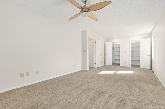 unfurnished bedroom featuring a spacious closet, a textured ceiling, light colored carpet, and ceiling fan