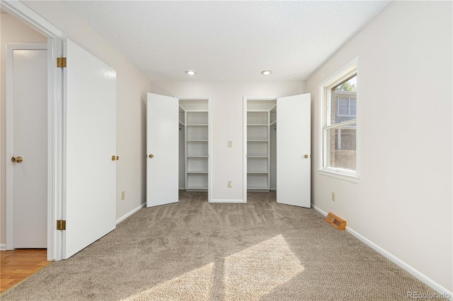 unfurnished bedroom with a walk in closet, a textured ceiling, and light colored carpet