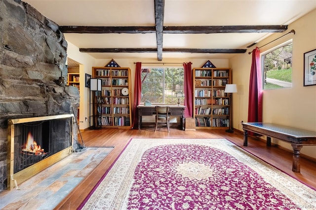 sitting room featuring a stone fireplace, baseboards, wood finished floors, and beam ceiling