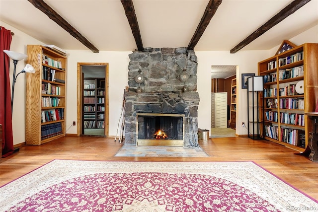 sitting room featuring a stone fireplace, baseboards, wood finished floors, and beamed ceiling