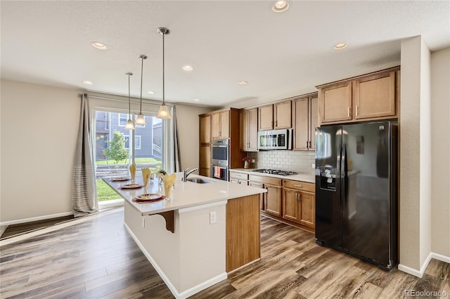 kitchen featuring hardwood / wood-style floors, an island with sink, pendant lighting, a breakfast bar area, and appliances with stainless steel finishes