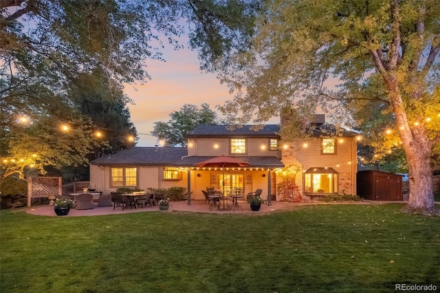 back house at dusk with a lawn, a patio, and a shed