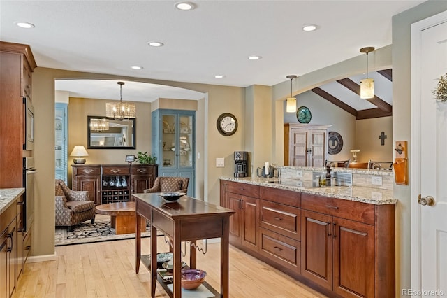 interior space with hanging light fixtures, vaulted ceiling with beams, light stone countertops, appliances with stainless steel finishes, and light hardwood / wood-style floors