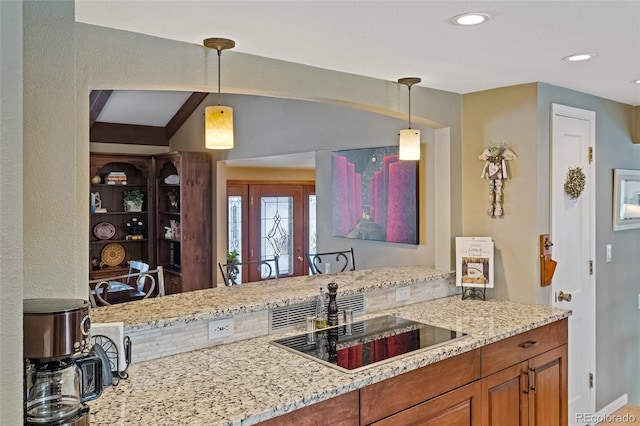 kitchen with light stone countertops, black electric cooktop, and hanging light fixtures