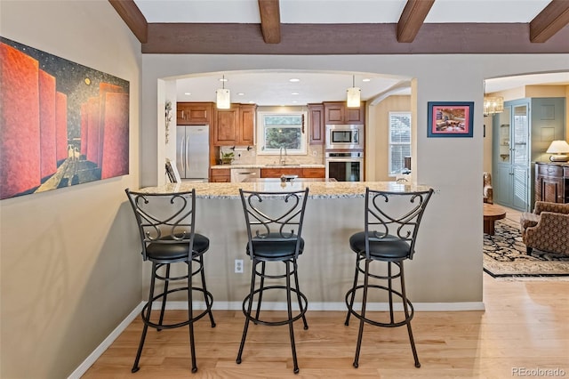 kitchen with beam ceiling, kitchen peninsula, stainless steel appliances, and a breakfast bar area