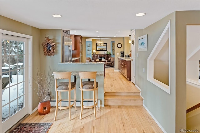 kitchen featuring a kitchen bar, stainless steel fridge, kitchen peninsula, light stone counters, and light hardwood / wood-style floors