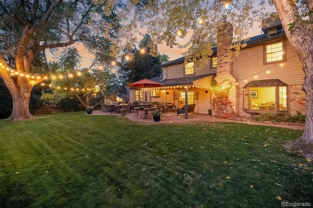 back house at dusk with a patio area and a yard