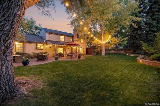 back house at dusk with a yard and a patio