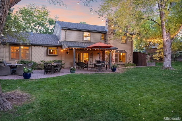 back house at dusk featuring a lawn, a patio area, and a storage shed