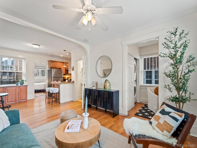 living room featuring arched walkways, ornamental molding, a ceiling fan, and light wood finished floors