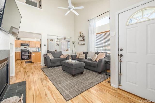 living room with a tiled fireplace, sink, a high ceiling, and light wood-type flooring