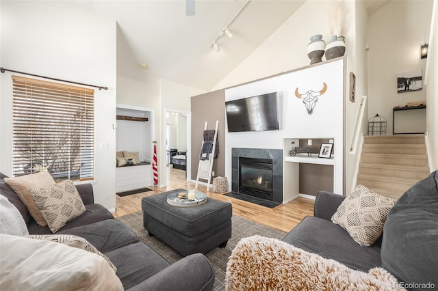 living room featuring a tiled fireplace, vaulted ceiling, track lighting, and light hardwood / wood-style floors