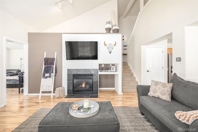 living room featuring wood-type flooring, rail lighting, a tiled fireplace, and vaulted ceiling