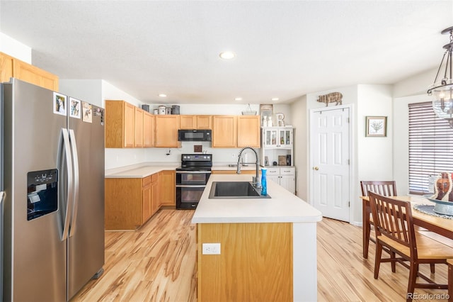 kitchen featuring pendant lighting, sink, black appliances, a center island with sink, and light wood-type flooring