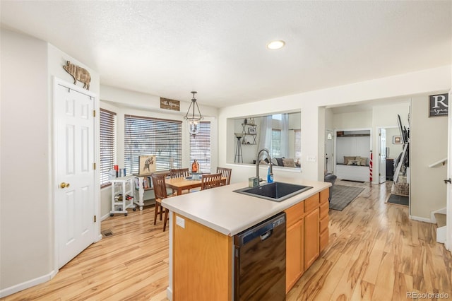 kitchen featuring an island with sink, black dishwasher, sink, hanging light fixtures, and light hardwood / wood-style floors