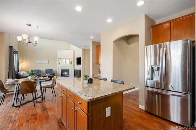 7624 Russell Ct, Arvada, CO 80007 - kitchen featuring stainless steel fridge with ice dispenser, dark wood-style floors, a center island, brown cabinetry, and light stone counters