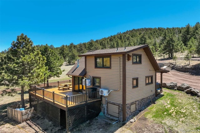 rear view of house with a forest view, a deck, a garage, and stone siding