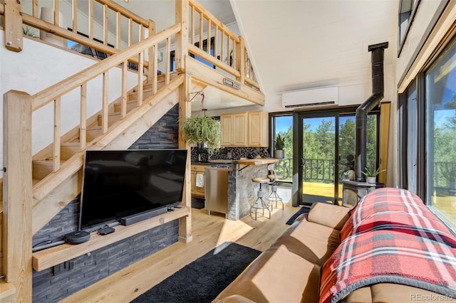 living room with a wall mounted AC, wood finished floors, plenty of natural light, high vaulted ceiling, and a wood stove