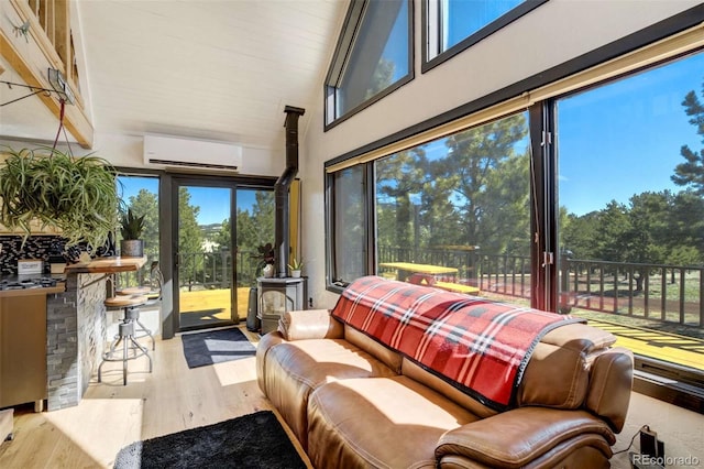 sunroom with a wall unit AC, a wood stove, wood finished floors, and a high ceiling