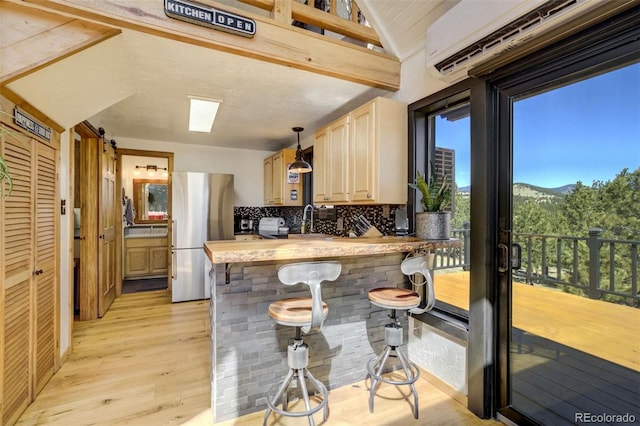 kitchen featuring freestanding refrigerator, a wall mounted AC, light wood-style floors, tasteful backsplash, and lofted ceiling